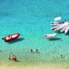 Mare cristallino con gommoni e bagnanti in spiaggia.