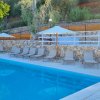Piscina con lettini sotto ombrelloni bianchi, circondata da alberi.