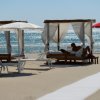 Spiaggia con lettini sotto ombrelloni e tende di vimini. Mare scintillante sullo sfondo.