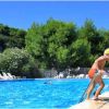 Un bambino con cuffia gialla esce da una piscina all'aperto circondata da alberi.
