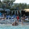 Spiaggia affollata con sdraio blu, ombrelloni di paglia e persone in relax.