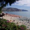 Lunga spiaggia con ombrelloni organizzati, mare calmo e montagne sullo sfondo.
