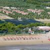 Spiaggia con ombrelloni arancioni, mare e colline con villette.