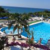 Piscina con vista mare, persone in acqua, palme e ombrelloni blu.