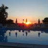 Piscina al tramonto con ombrelloni riflessi nell'acqua.
