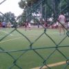 Persone che giocano a calcio su un campo, viste attraverso una rete.