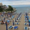 Spiaggia con lettini blu e ombrelloni chiusi, mare sullo sfondo.