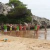 Bambini fanno esercizi sulla spiaggia vicino a rocce e alberi.