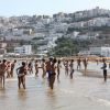 Persone in acqua su una spiaggia, case bianche sulla collina.